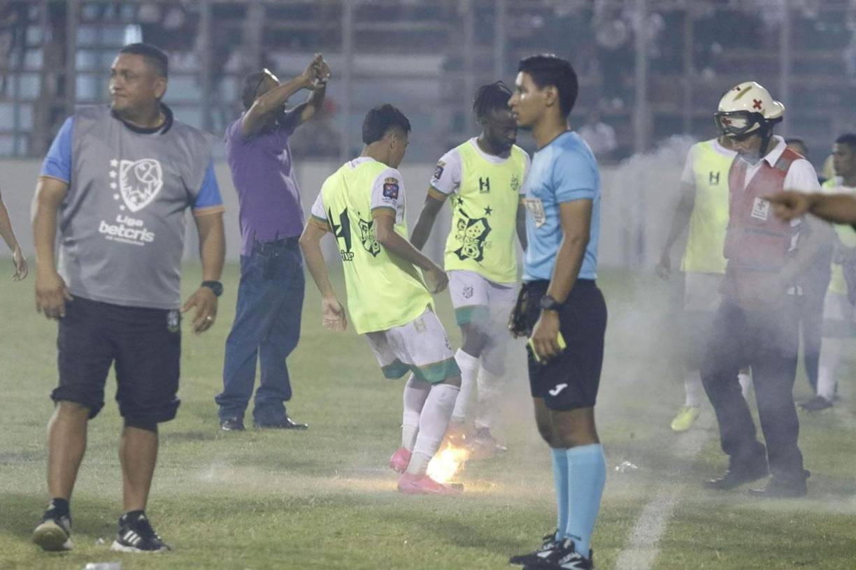Un jugador del Platense tratando de sacar una de las bengalas del campo con los pies.