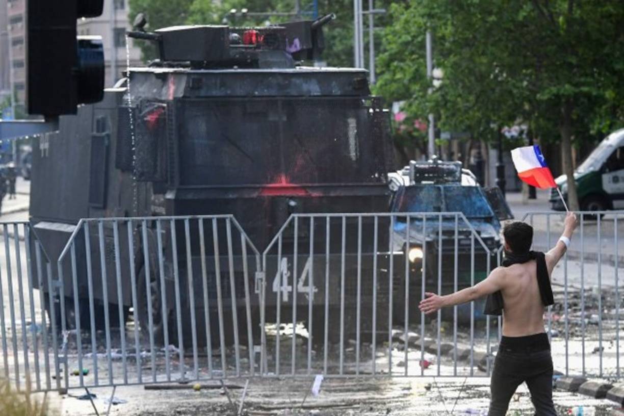 Entre la multitud comenzó a desplegarse una gigantesca bandera con el lema 'Chile despertó', la consigna que ha proliferado por las redes sociales, acompañado de la frase 'No estamos en guerra', en referencia a la declaración de guerra que hizo Piñera contra los causantes de incendios en supermercados y estaciones del Metro.