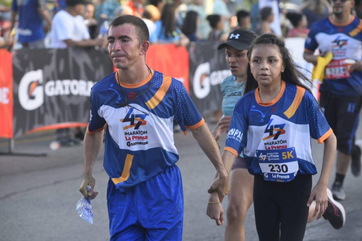 Un padre sujeta de la mano a su hija para ayudarla a llegar a la meta.