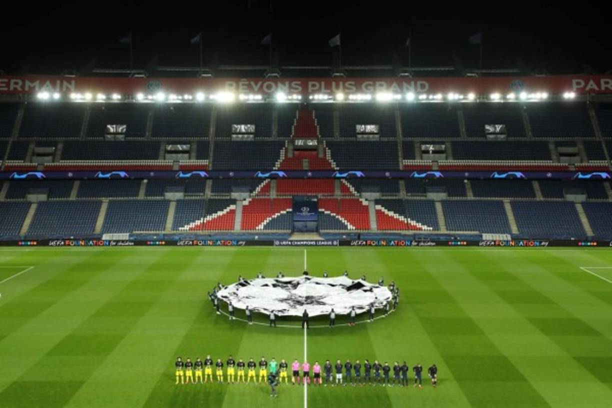Imagen panorámica del estadio Parque de los Príncipes, desierto en las gradas por el coronavirus. Los jugadores de PSG y Borussia Dortmund mientras suena el himno nacional de la Champions League.