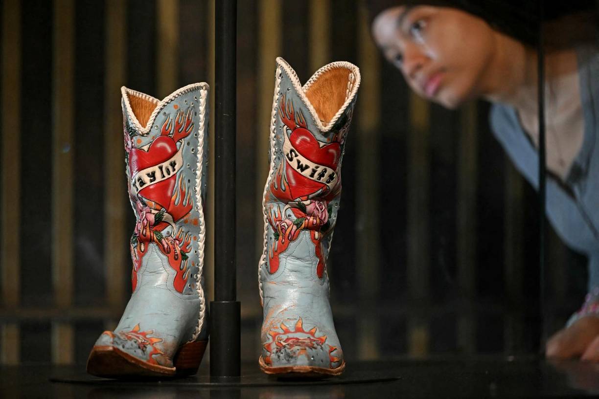 Una asistente de galería observa las botas de vaquero que lució la artista estadounidense Taylor Swift en su gira Soul2Soul II, diseñadas por Liberty Boot Co, durante una sesión fotográfica previa a la próxima exposición titulada ‘Taylor Swift | Songbook Trail’ en el Museo V&amp;A (Victoria and Albert) en Londres el 24 de julio de 2024. 