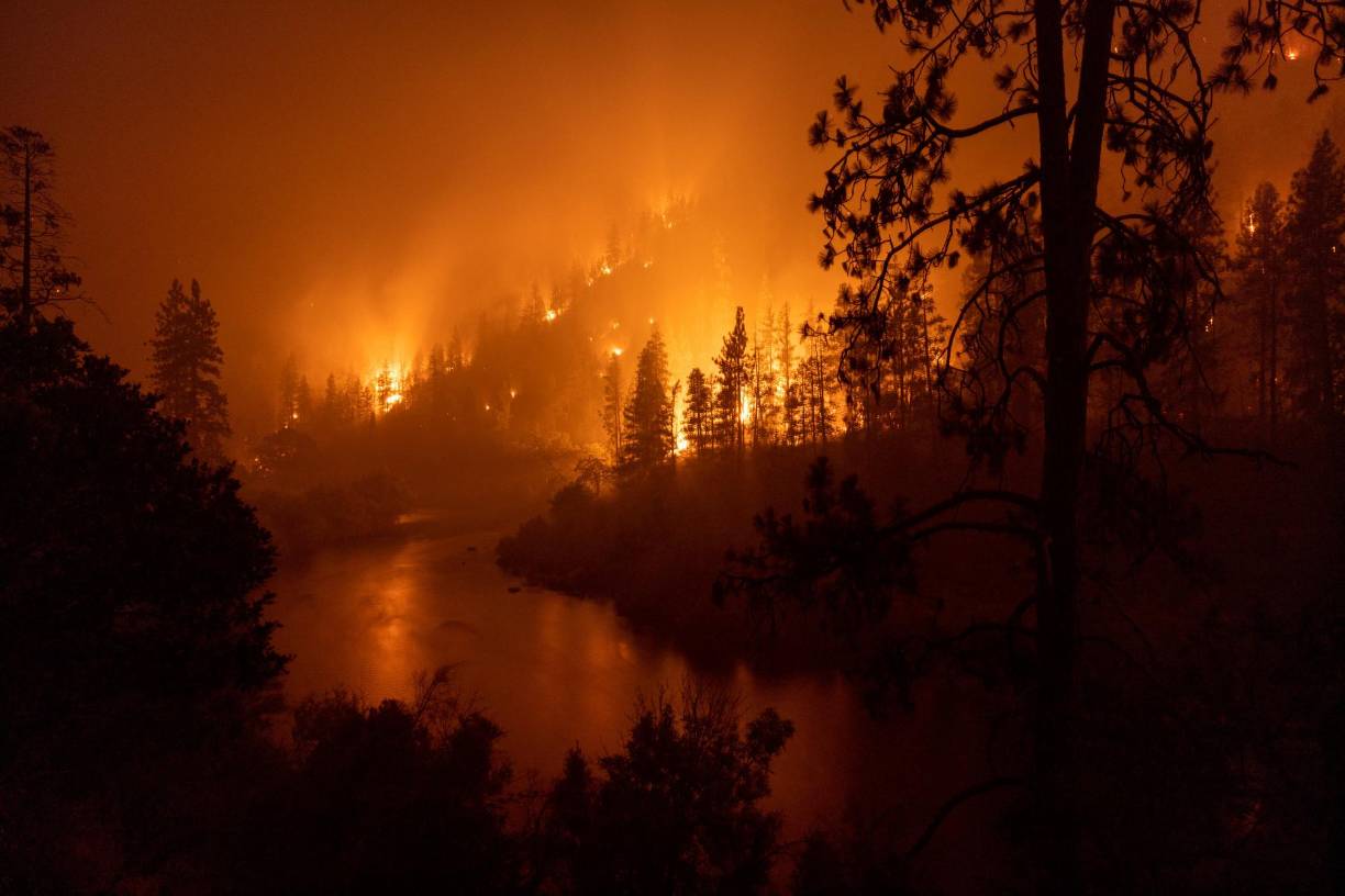 Flames burn to the Klamath River during the McKinney Fire in the Klamath National Forest northwest of Yreka, California, on July 31, 2022. - The largest fire in California this year is forcing thousands of people to evacuate as it destroys homes and rips through the state's dry terrain, whipped up by strong winds and lightning storms. The McKinney Fire was zero percent contained, CalFire said, spreading more than 51,000 acres near the city of Yreka. (Photo by DAVID MCNEW / AFP)