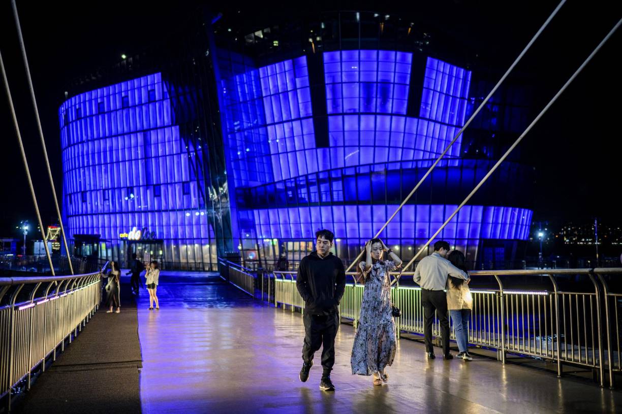 Personas caminan frente a las islas flotantes del parque Banpo Hangang, que están iluminadas con luz púrpura, color que identifica el grupo surcoreano.