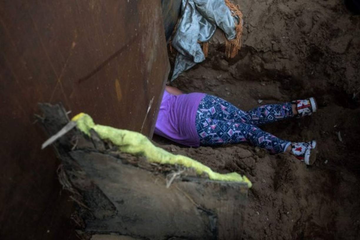 Honduran migrant Andrea Nicolle, 10, travelling in a caravan of Central American migrants hoping to get to the United States, crosses through a hole on the ground under the metal barrier separating Mexico and the US to cross from Playas de Tijuana in Mexico into the US, on December 4, 2018. - Mexico's new Foreign Minister Marcelo Ebrard met with US Secretary of State Mike Pompeo for a 'friendly' meeting amid tensions over the migrant crisis at the border. Both countries are grappling with how to handle the thousands of Central American migrants who are camped at the common border -- in the short and long terms. (Photo by Guillermo Arias / AFP)