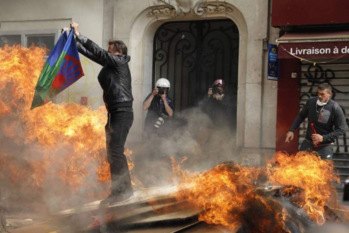Un manifestante sostiene una bandera del pueblo romaní mientras se para sobre tablas en llamas.