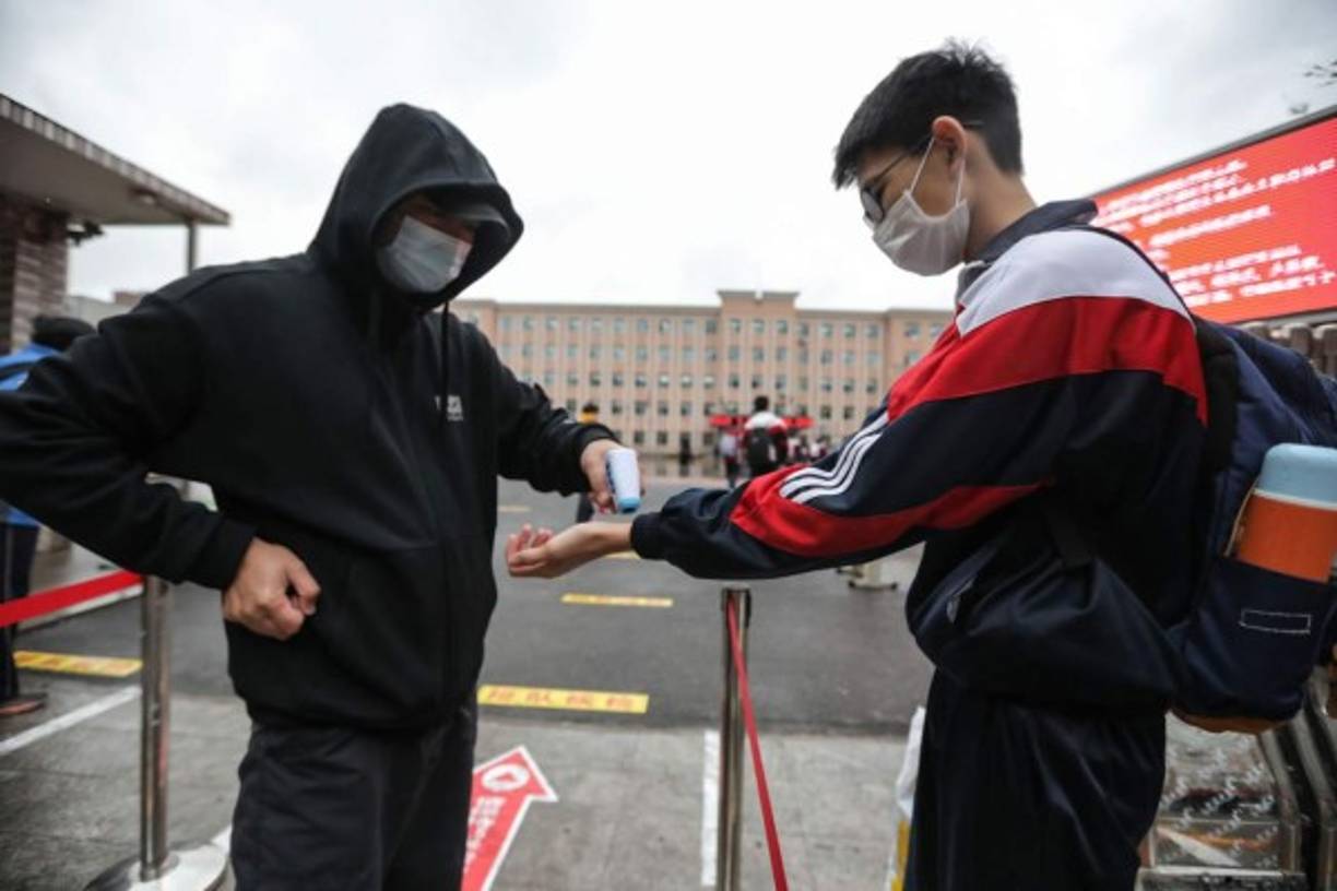 Un miembro del personal verifica la temperatura corporal de un estudiante a la entrada de una escuela, en Yantai, en la provincia oriental china de Shandong.