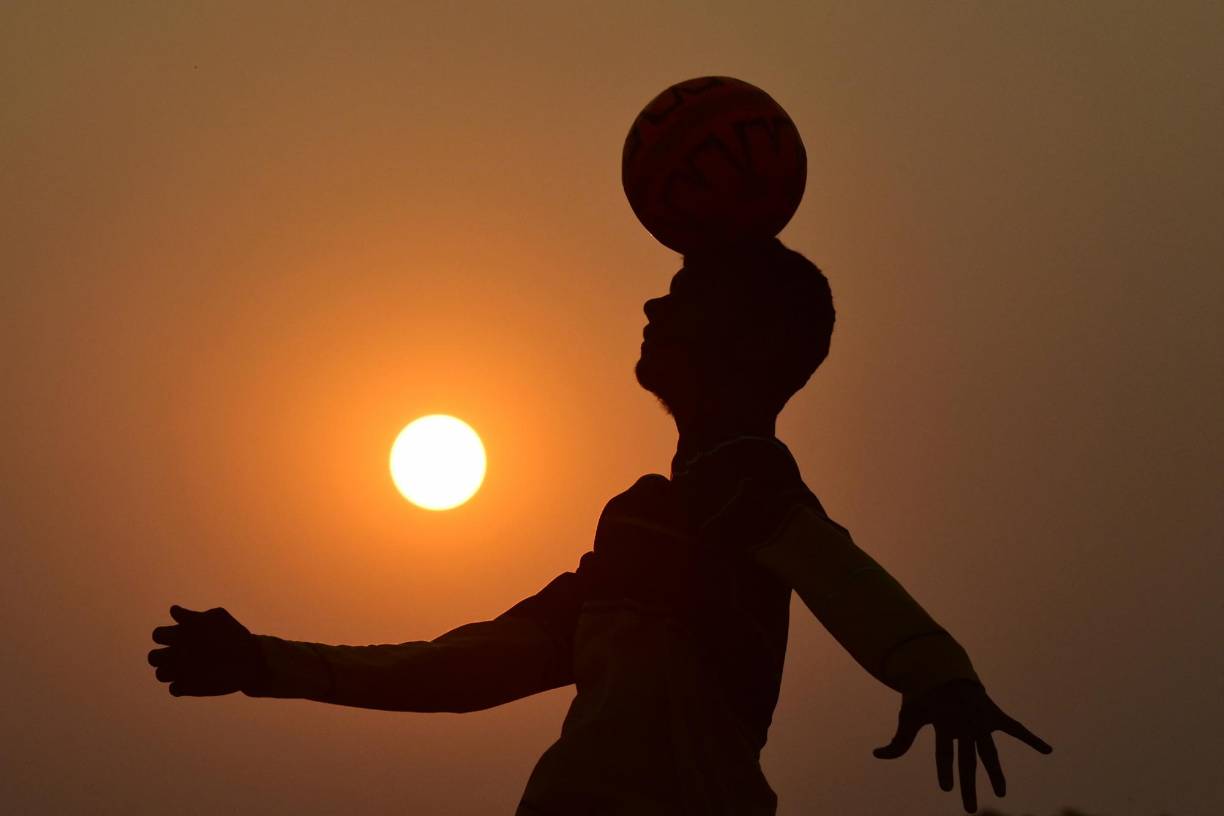 Un niño juega fútbol en un campo, antes del torneo de fútbol de la Copa Mundial de la FIFA, en Prayagraj.