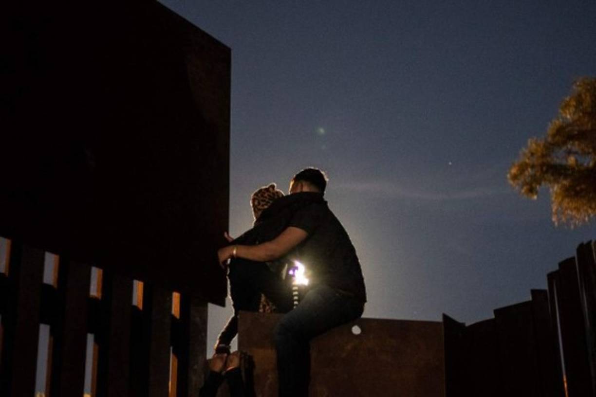 A girl who has been traveling in a caravan of Central American migrants hoping to get to the United States, is helped to climb the metal barrier separating Mexico and the US to cross from Playas de Tijuana in Mexico into the US, on December 3, 2018. - Thousands of Central American migrants, mostly Hondurans, have trekked for over a month in the hopes of reaching the United States. (Photo by Guillermo Arias / AFP)
