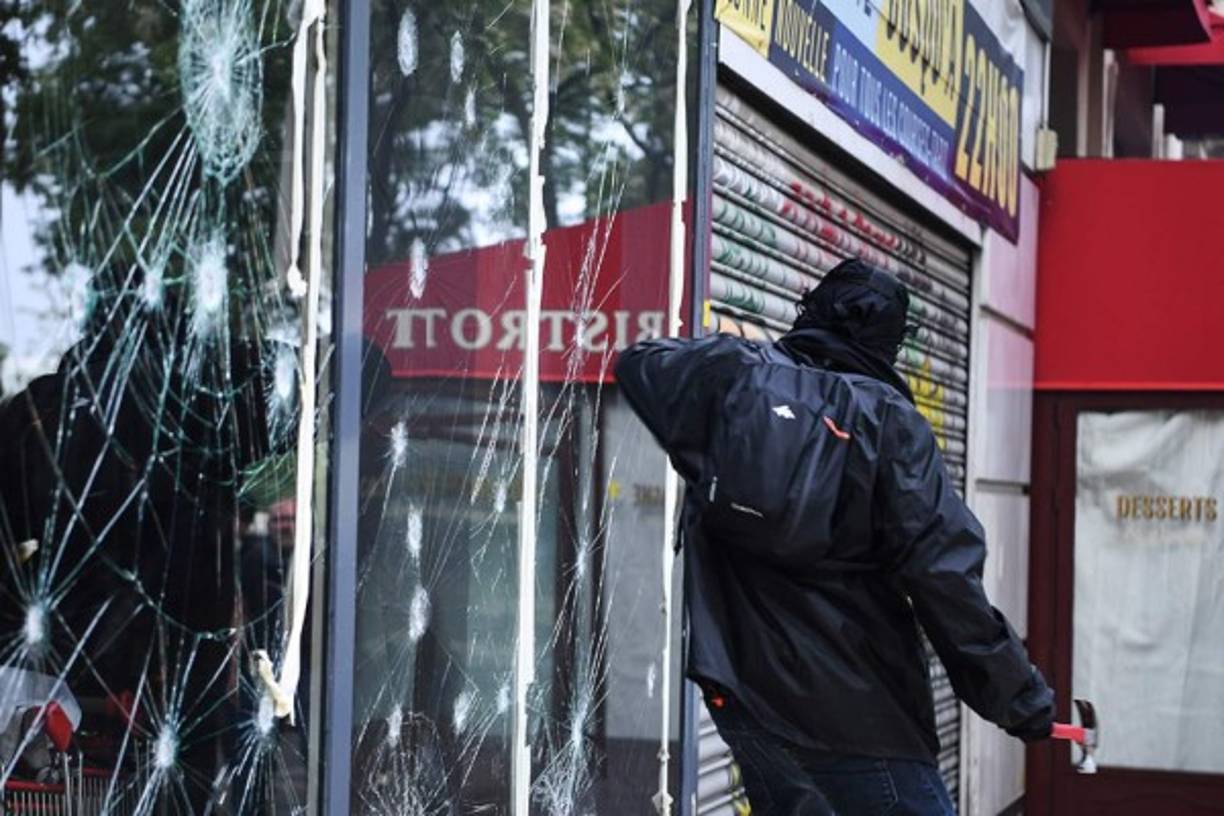 FRANCIA. Un manifestante enmascarado vestido de negro destroza un escaparate con un martillo al margen de la manifestación