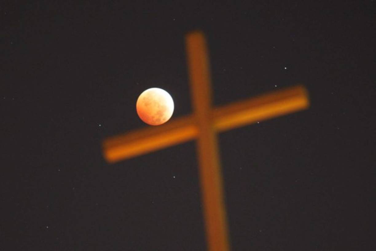 Una cruz religiosa es vista junto a la Luna que está iluminada por la luz solar reflejada por la Tierra durante un eclipse total lunar el 8 de octubre de 2014 en Los Angeles, California. AFP