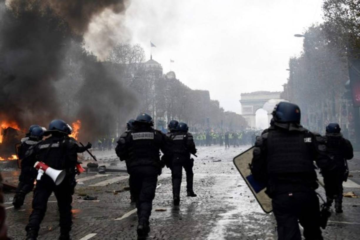 Riot police run during a protest of Yellow vests (Gilets jaunes) against rising oil prices and living costs near the Arc of Triomphe on the Champs Elysees in Paris, on November 24, 2018. - Police fired tear gas and water cannon on November 24 in central Paris against 'yellow vest' protesters demanding French President Emmanuel Macron roll back tax hikes on motor fuel. (Photo by Bertrand GUAY / AFP)