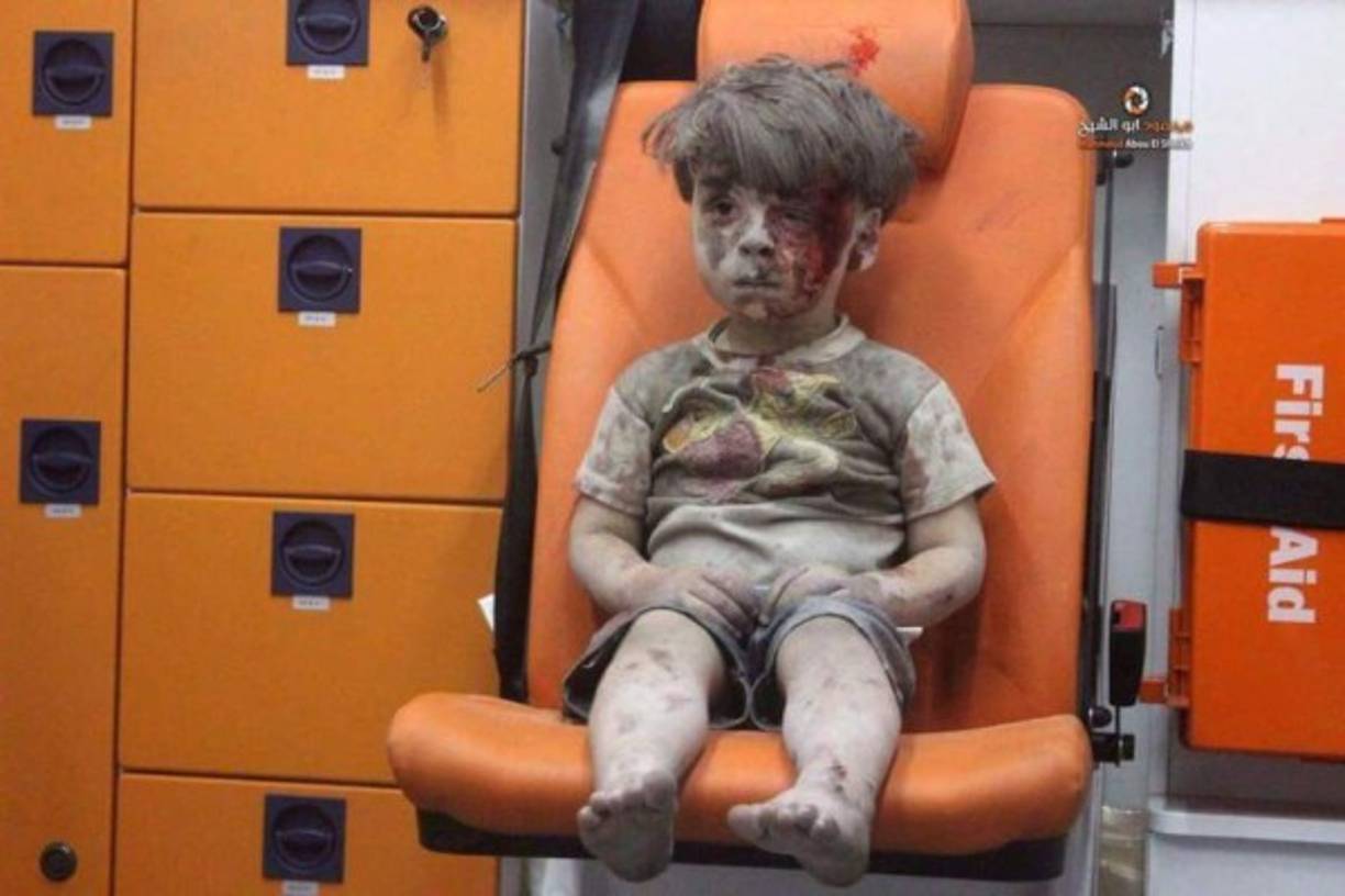 La foto de un niño de 5 años llamado Omran, que resultó herido en los bombardeos a la ciudad siria de Alepo, ha puesto hoy de nuevo rostro al drama que sufren los civiles a causa del devastador conflicto en el país árabe. Con el rostro cubierto de sangre y polvo, el menor aparece sentado en una ambulancia tras ser rescatado anoche de una vivienda bombardeada en el barrio de Al Qatergui. La imagen es un fotograma de un video publicado en internet por los activistas del Centro de Información de Alepo, que ya tiene más de 81.000 vistas. El video muestra a uno de los miembros de la Defensa Civil saliendo de entre los escombros de la vivienda con Omran en brazos, entre los gritos habituales de 'Alá es grande' y 'ya haram' (qué pecado, en alusión al bombardeo).