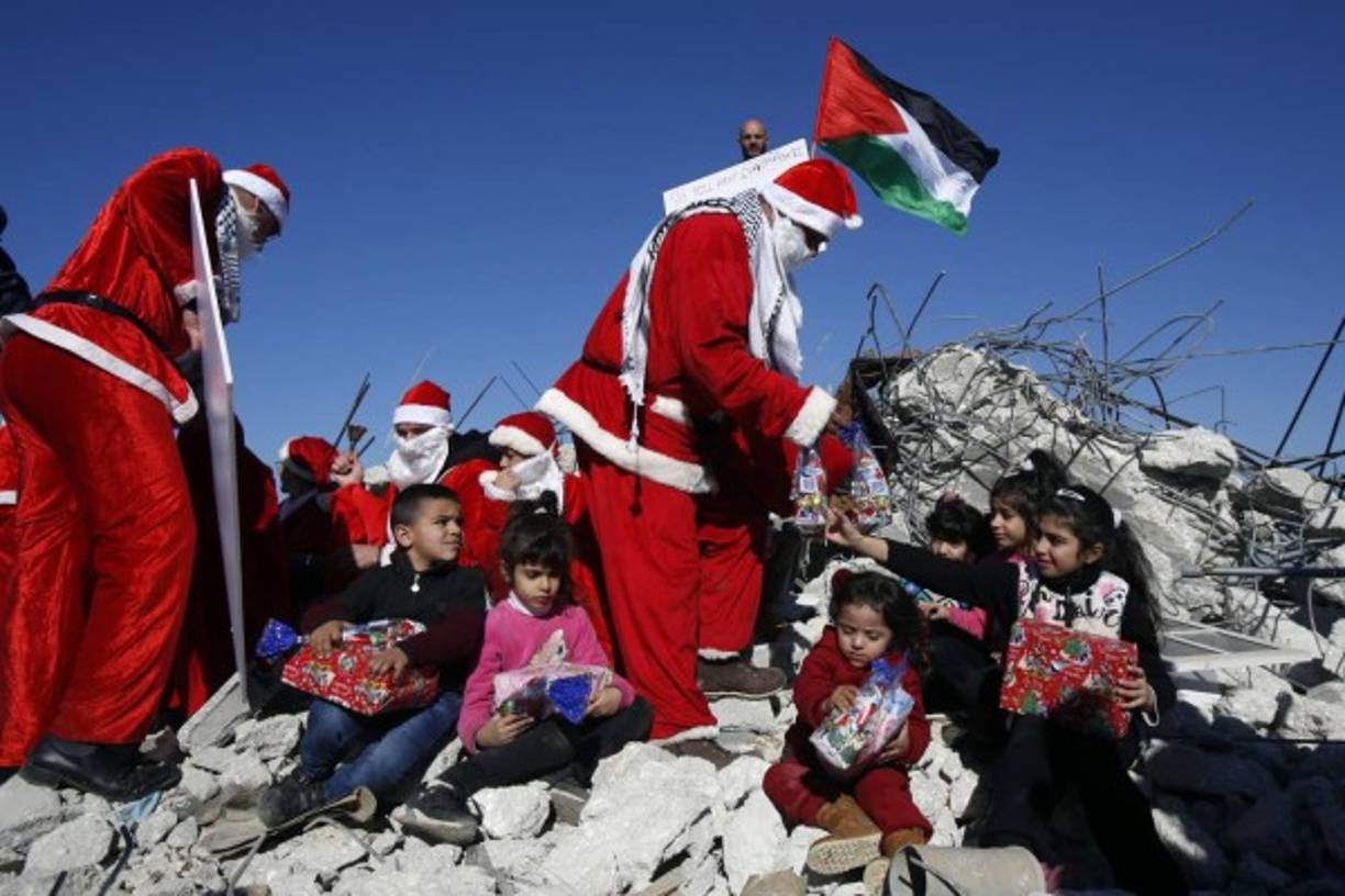 Los palestinos vestidos con trajes de Navidad distribuyeron regalos a los niños sentados sobre los escombros de una casa demolida por Israel.