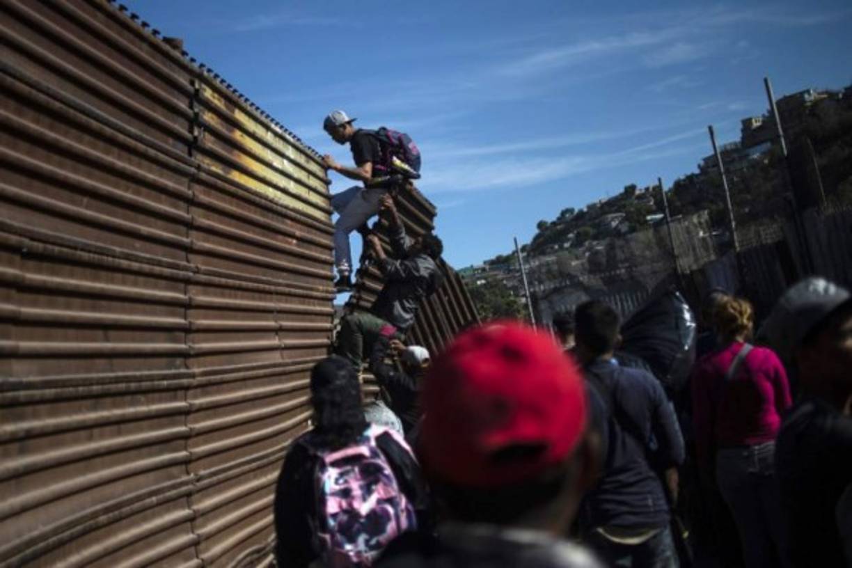 A group of Central American migrants -mostly Hondurans- climb the border fence between Mexico and the United States, near El Chaparral border crossing, in Tijuana, Baja California State, Mexico, on November 25, 2018. - Hundreds of migrants attempted to storm a border fence separating Mexico from the US on Sunday amid mounting fears they will be kept in Mexico while their applications for a asylum are processed. An AFP photographer said the migrants broke away from a peaceful march at a border bridge and tried to climb over a metal border barrier in the attempt to enter the United States. (Photo by Pedro PARDO / AFP)