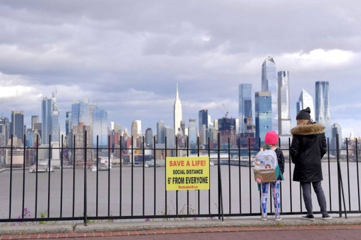 Una mujer y una niña miran la vista de Manhattan, de pie junto a una de las muchas señales de distancia social . AFP