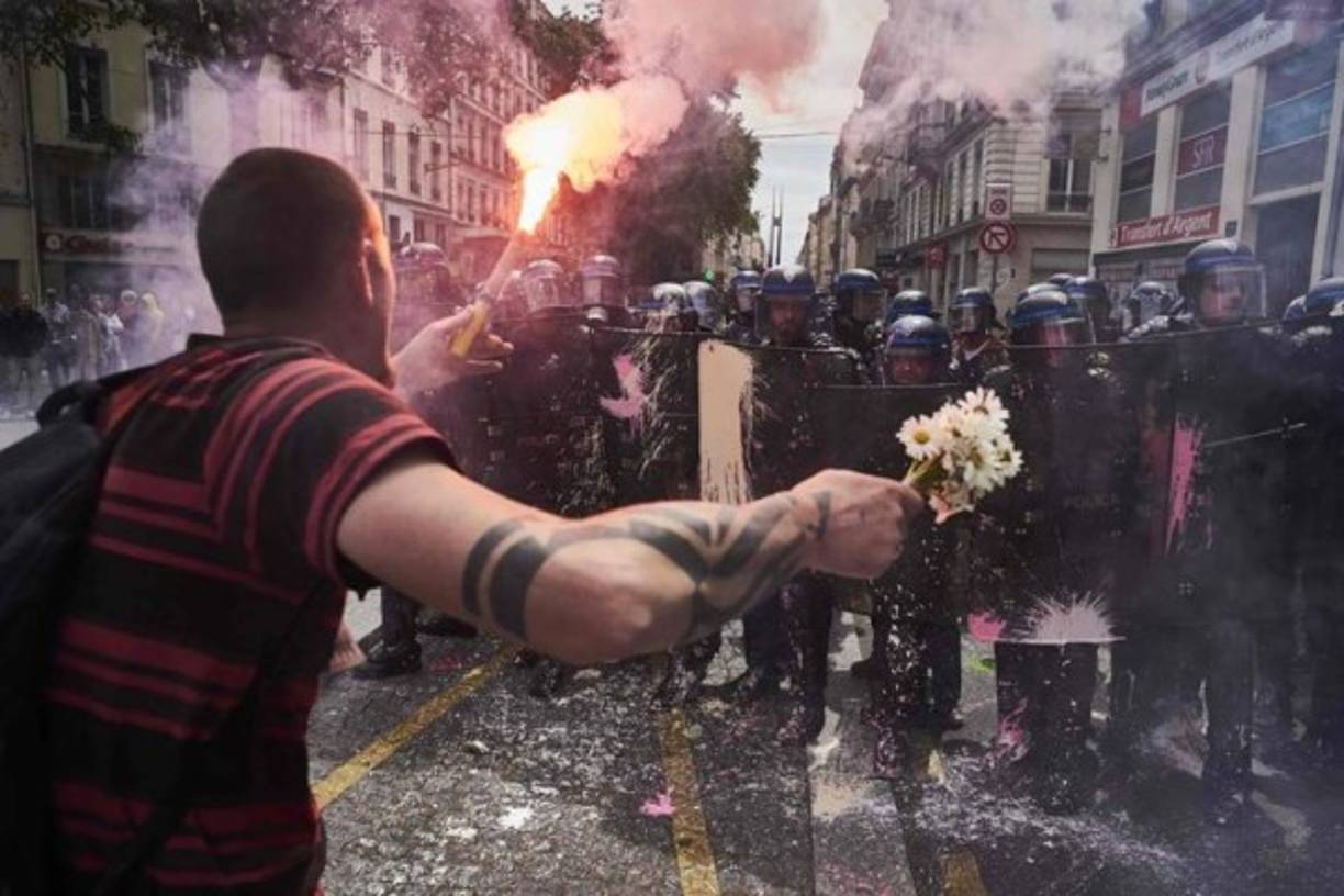 Un hombre sostiene un ramo de flores y una antorcha mientras se enfrenta a la policía antidisturbios durante una manifestación contra la reforma laboral planificada por el gobierno francés , el 26 de mayo de 2016 en Lyon, en el centro-este de Francia.