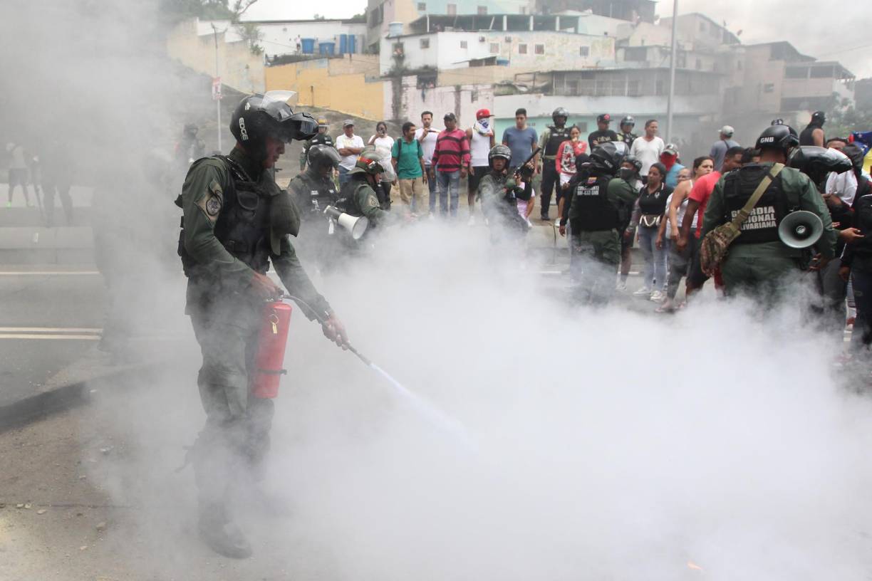 Un integrante de la Guardia Nacional Bolivariana (GNB) extingue el fuego de neumáticos quemados por manifestantes luego de los resultados de las elecciones presidenciales este lunes, en el sector del Primero de Mayo en Caracas. 