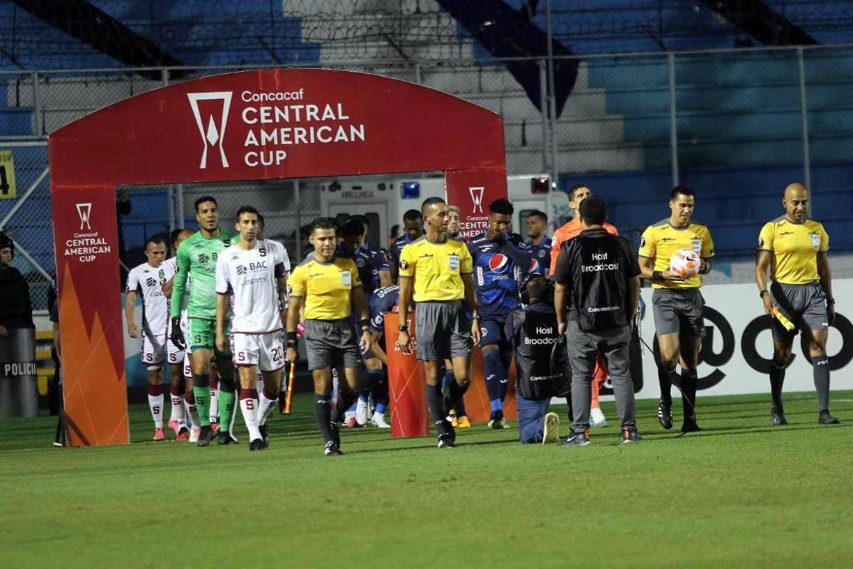 La salida de los equipos de Motagua y Saprissa encabezados por la cuarteta arbitral del partido.