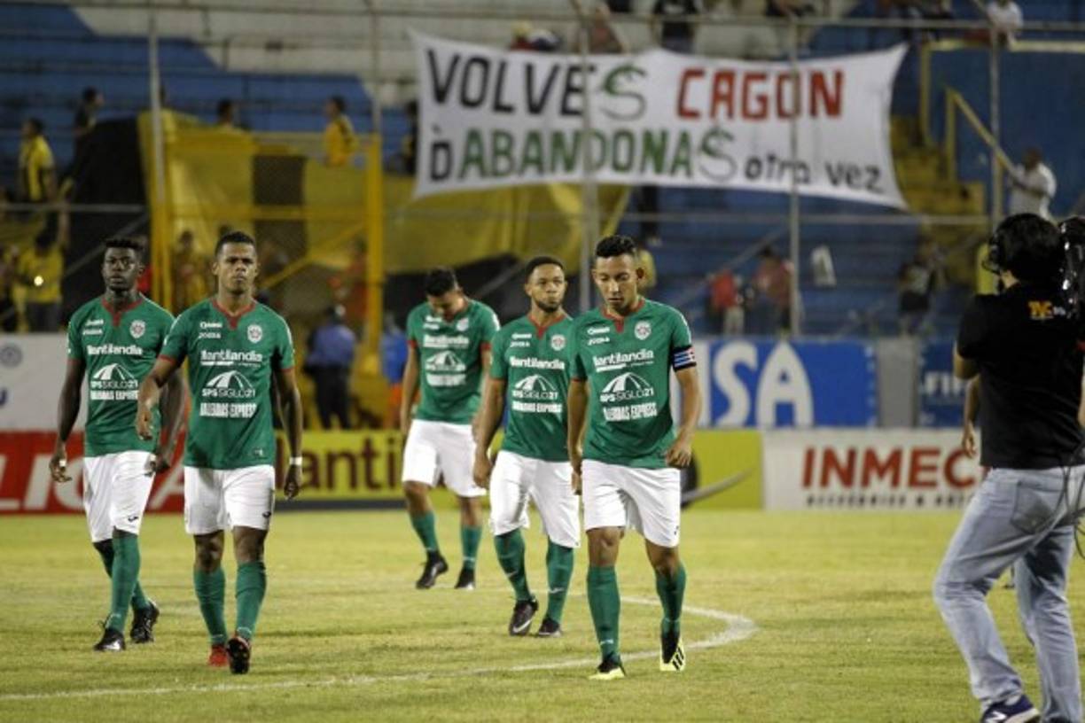 Los jugadores del Marathón, cabizbajos al final del partido y al fondo una pancarta de la barra del Real España contra los verdolagas.