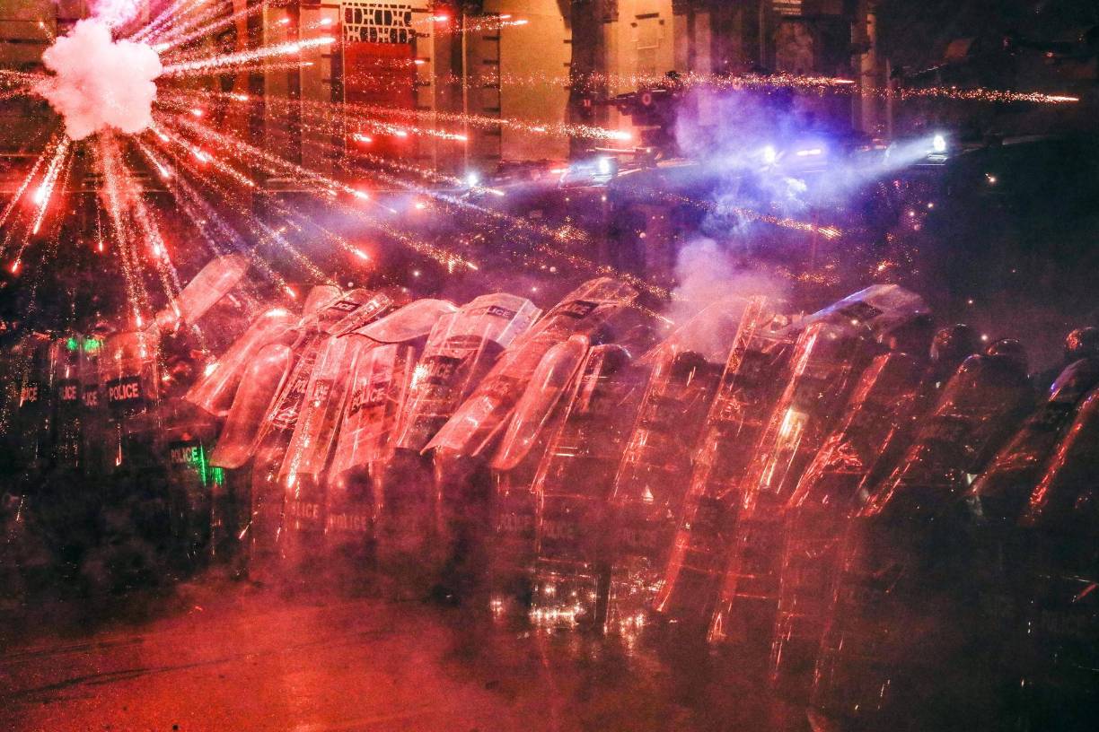 Antidisturbios se protegen de los fuegos artificiales lanzados por opositores durante una protesta frente al Parlamento en Tiflis, Georgia, el 3 de diciembre. 