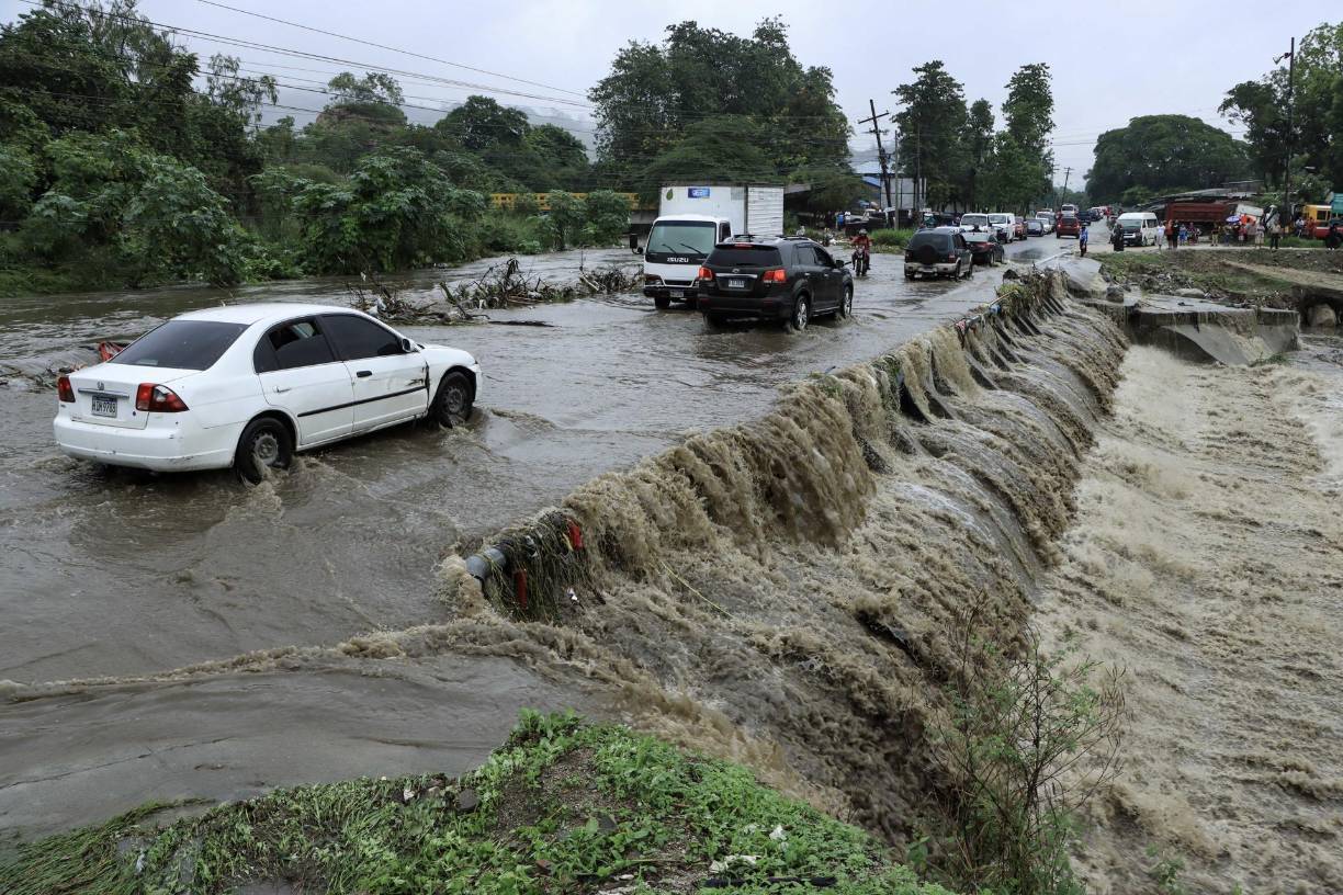 Residentes hondureños transitan por una creciente de agua de una quebrada hoy en la ciudad de San Pedro Sula (Honduras).