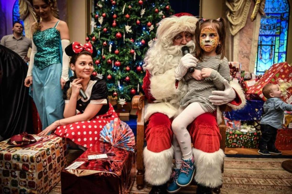 Decenas de Santa Claus alegran la Navidad a los niños del mundo. En la foto, una niña comparte con el personaje en Bucarest, Rumania.