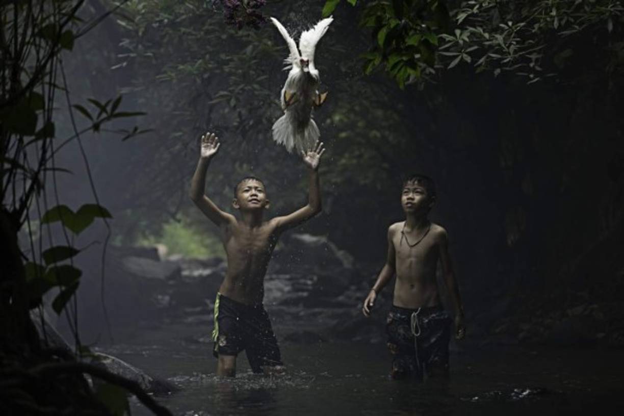 Dos niños tratando de atrapar un parto en un arroyo de Tailandia.