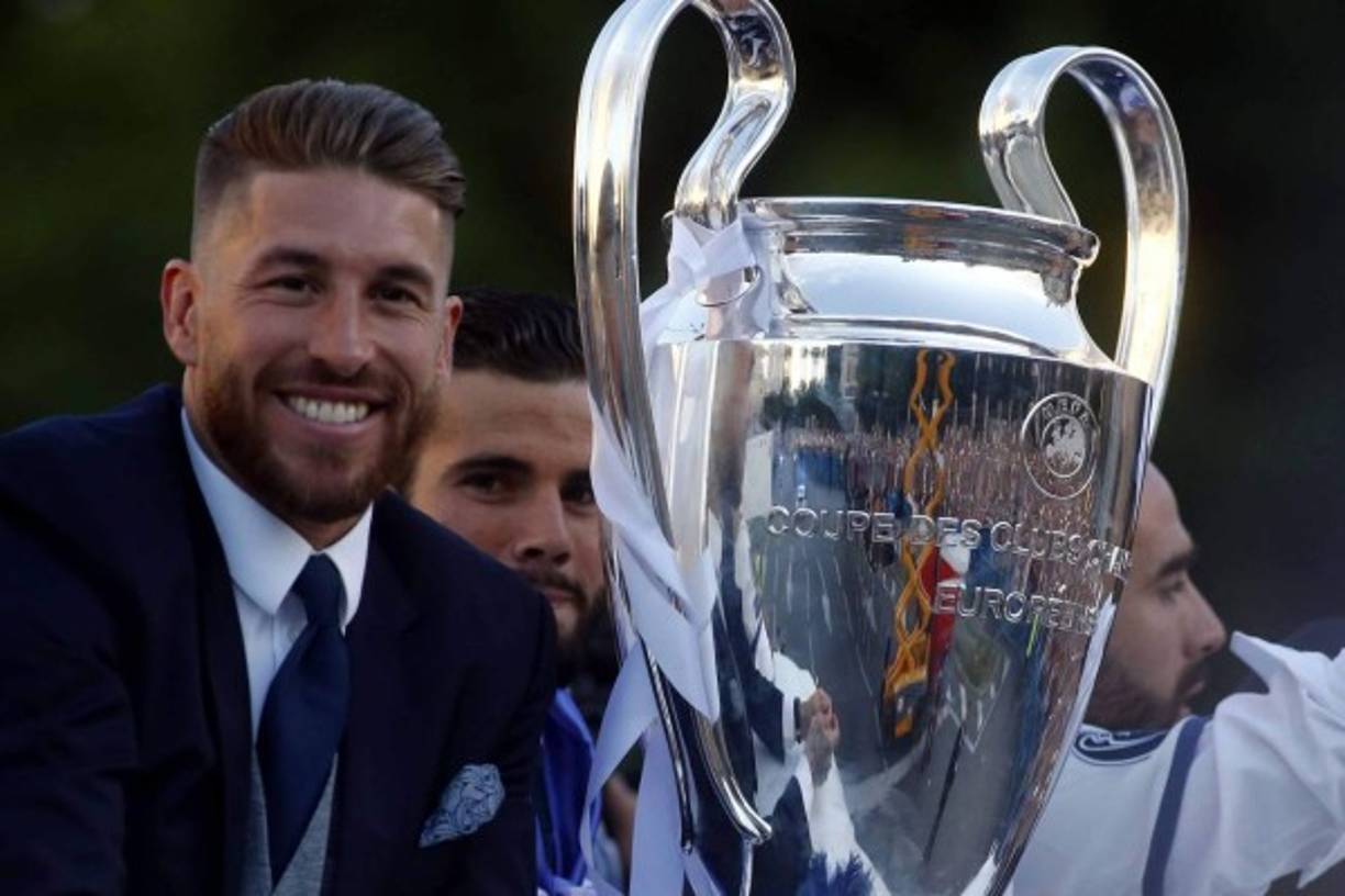 Real Madrid's defender Sergio Ramos (L) smiles beside the trophy celebrating the team's win from an onpen decker bus on Plaza Cibeles in Madrid on June 4, 2017 after the UEFA Champions League football match final Juventus vs Real Madrid CF held at the National Stadium of Wales in Cardiff on June 3, 2017. / AFP PHOTO / OSCAR DEL POZO