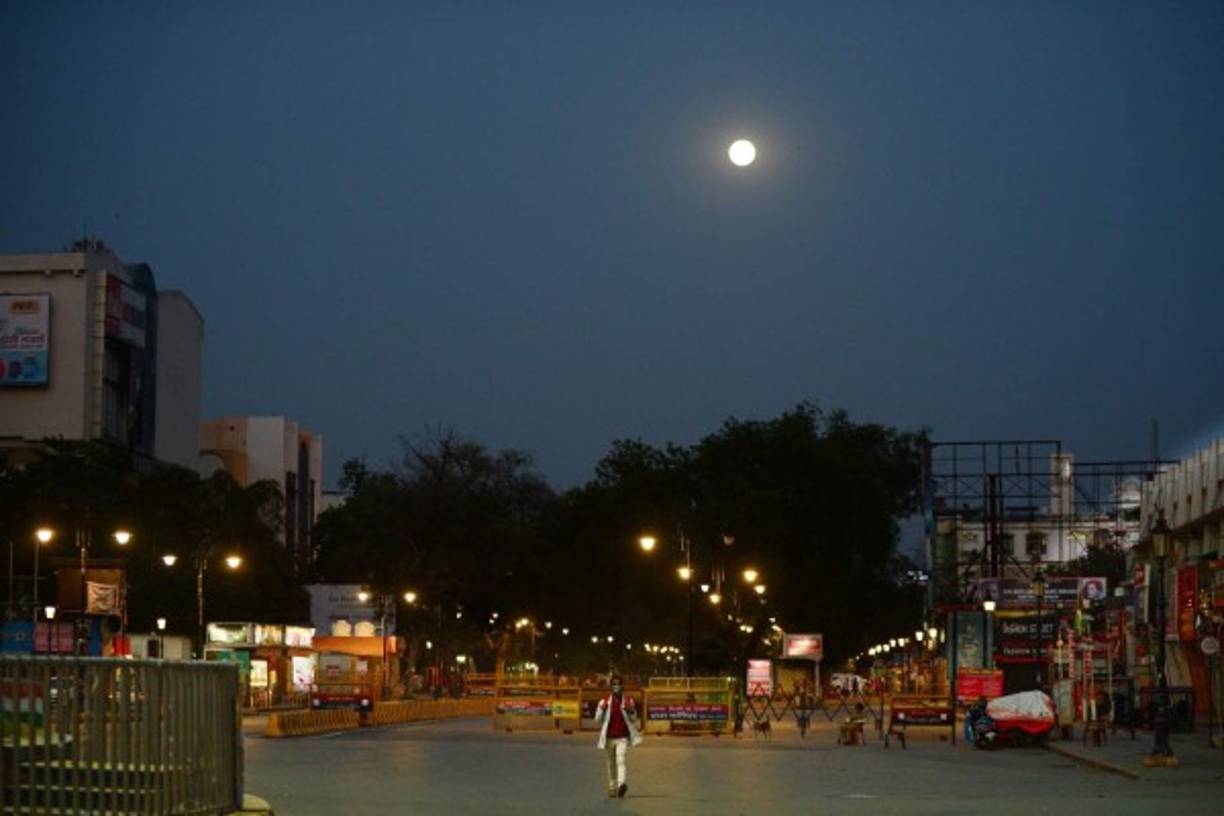 The full moon is seen as a man wearing a facemask walks along a deserted road during a government-imposed nationwide lockdown as a preventive measure against the COVID-19 coronavirus, in Allahabad on April 7, 2020. (Photo by SANJAY KANOJIA / AFP)
