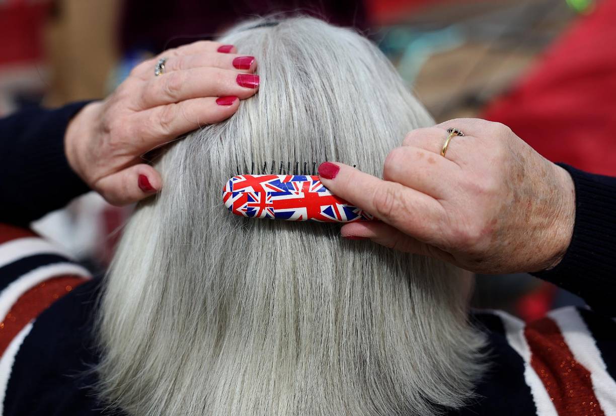 Una señora se peina el cabello mientras acampa en Londres; hay mucho optimismo con los nuevos reyes. 
