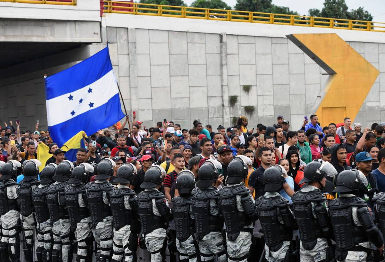 National Guard members stand guard as migrants from Central and South America with a Honduran flag take part in a caravan towards the border with the United States, in Tapachula, Chiapas state, Mexico, on June 6, 2022. (Photo by ISAAC GUZMAN / AFP)