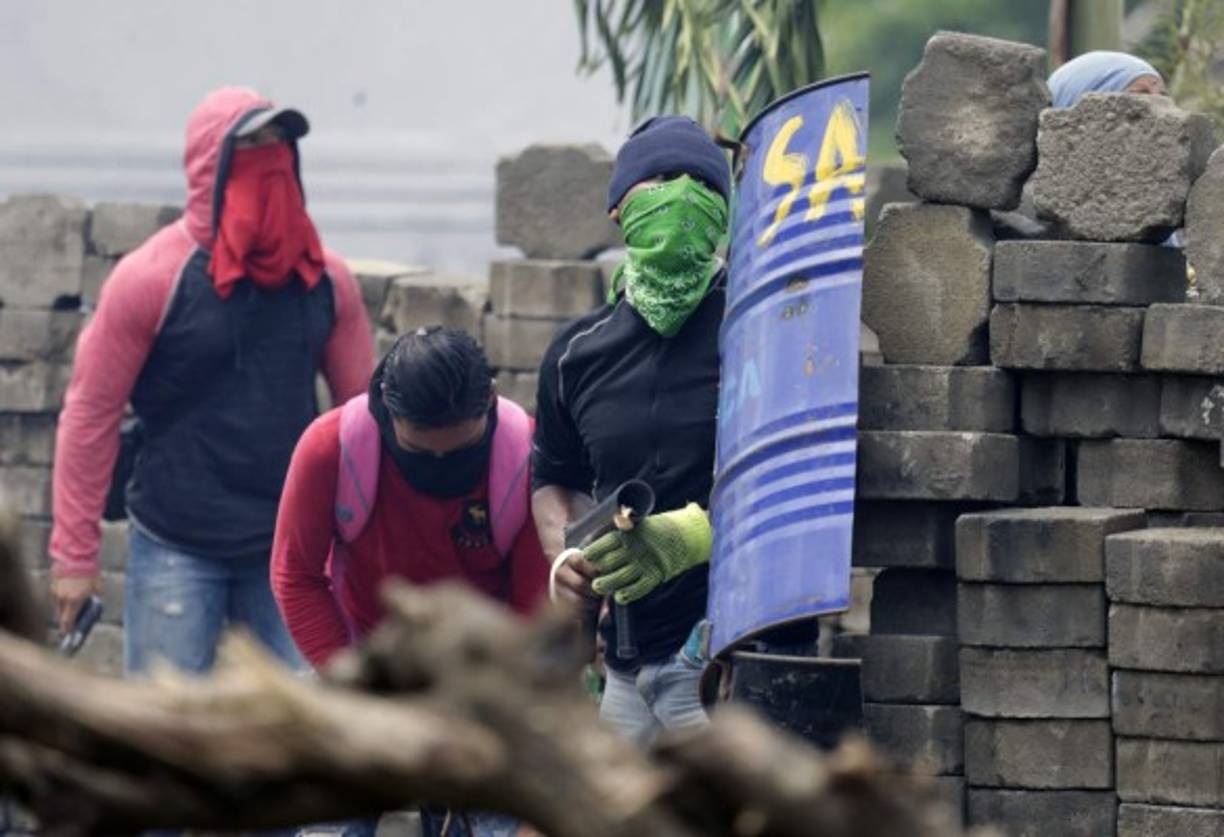 Anti-government demonstrators take cover behind a barricade, during clashes with riot police and members of the Sandinista youth, in Masaya some 35 km from Managua on June 19, 2018.<br/>Nicaraguan police and pro-government paramilitaries moved to reassert control over the city of Masaya by force Tuesday after residents of the opposition bastion declared themselves in rebellion against President Daniel Ortega. / AFP PHOTO / INTI OCON