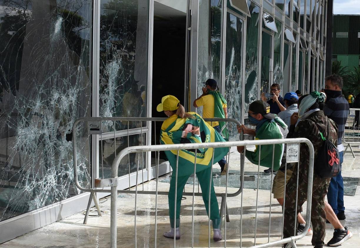 Supporters of Brazilian former President Jair Bolsonaro destroy a window of the the plenary of the Supreme Court in Brasilia on January 8, 2023. - Hundreds of supporters of Brazil's far-right ex-president Jair Bolsonaro broke through police barricades and stormed into Congress, the presidential palace and the Supreme Court Sunday, in a dramatic protest against President Luiz Inacio Lula da Silva's inauguration last week. (Photo by Ton MOLINA / AFP)