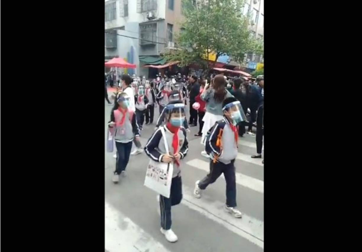 Niños de una escuela en China salen del edificio usando mascarillas y caretas transparentes.