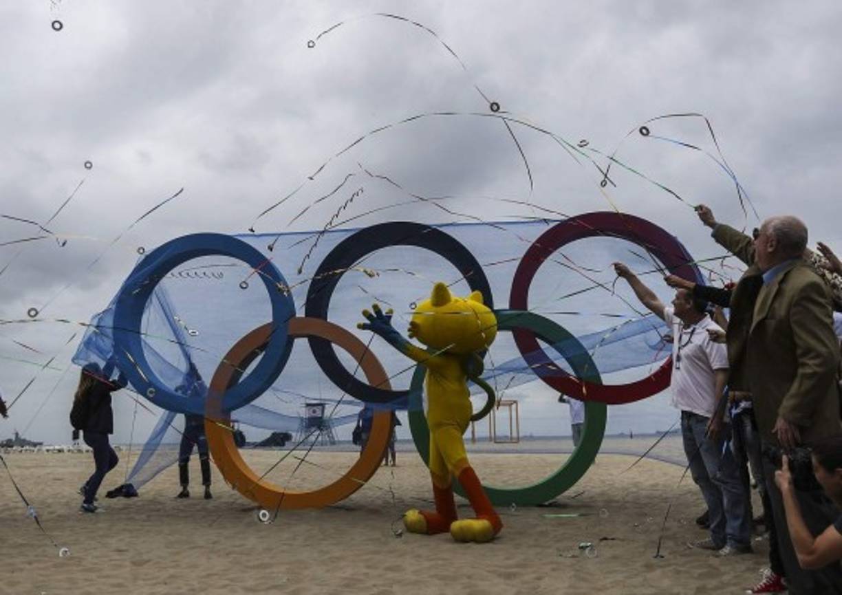 INAUGURACIÓN. Bienvenida a los Olímpicos. Un grupo de personas junto con Vinicius, (centro) la mascota de los juegos, lanzan papelillos durante la inauguración de los anillos olímpicos en la playa de Copacabana, Río de Janeiro. Foto: EFE/Antonio Lacerda.