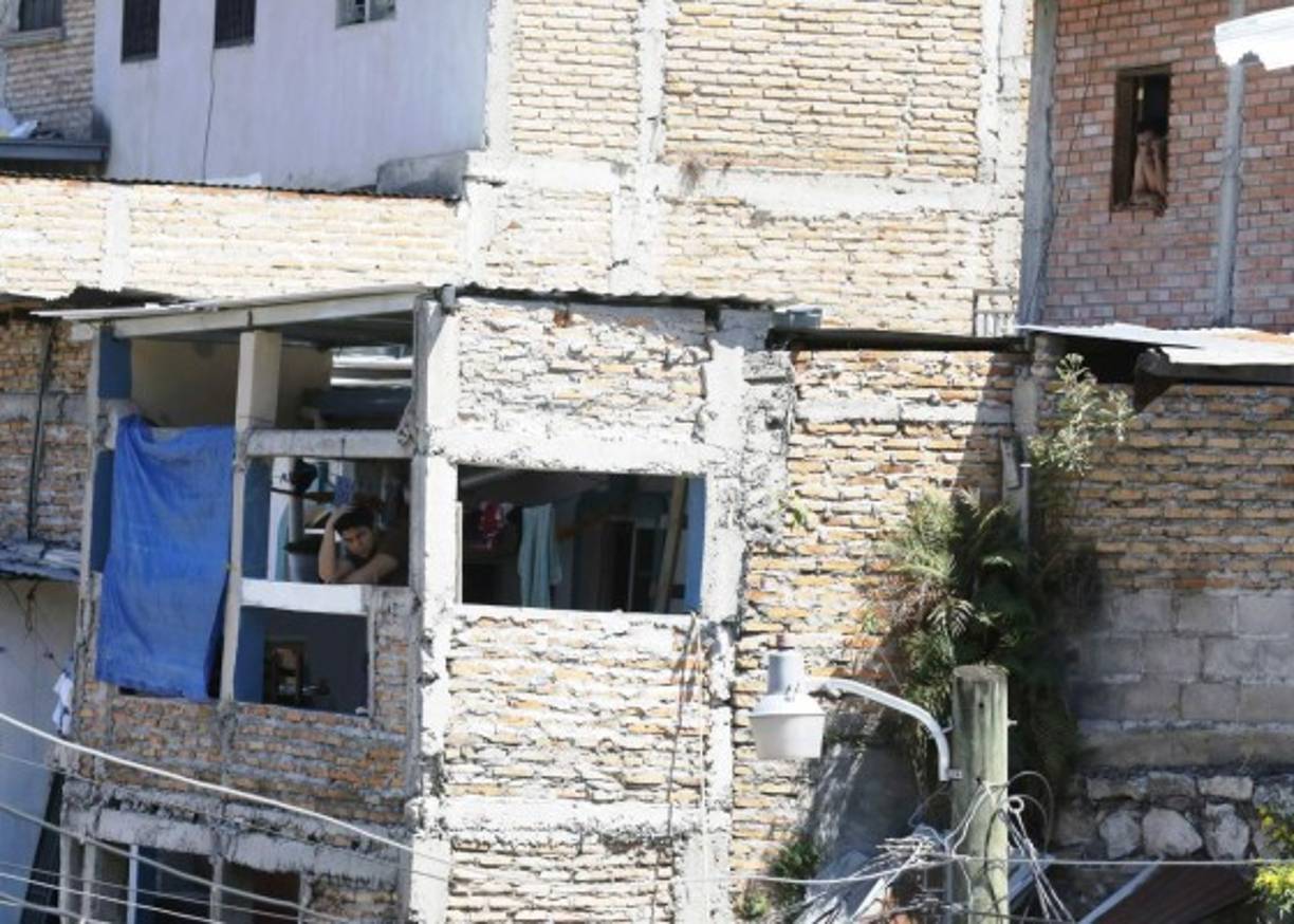 Dos hombres miran desde las ventanas de sus hogares el éxodo que se produjo en la colonia Las Torres de Tegucigalpa a causa de los grupos violentos.