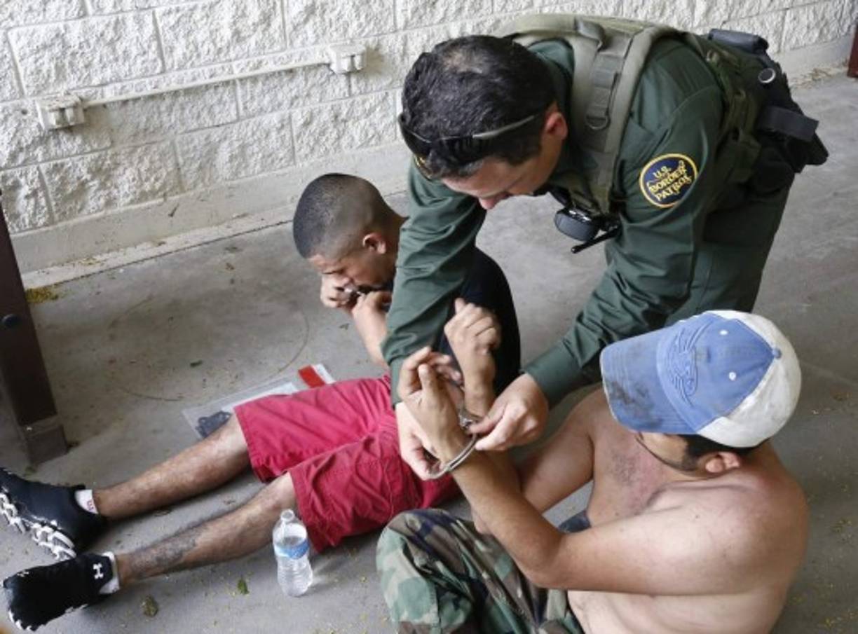 En la imagen, un agente de la Patrulla Fronteriza esposa a dos hombres sospechosos de haber cruzado el Río Grande.