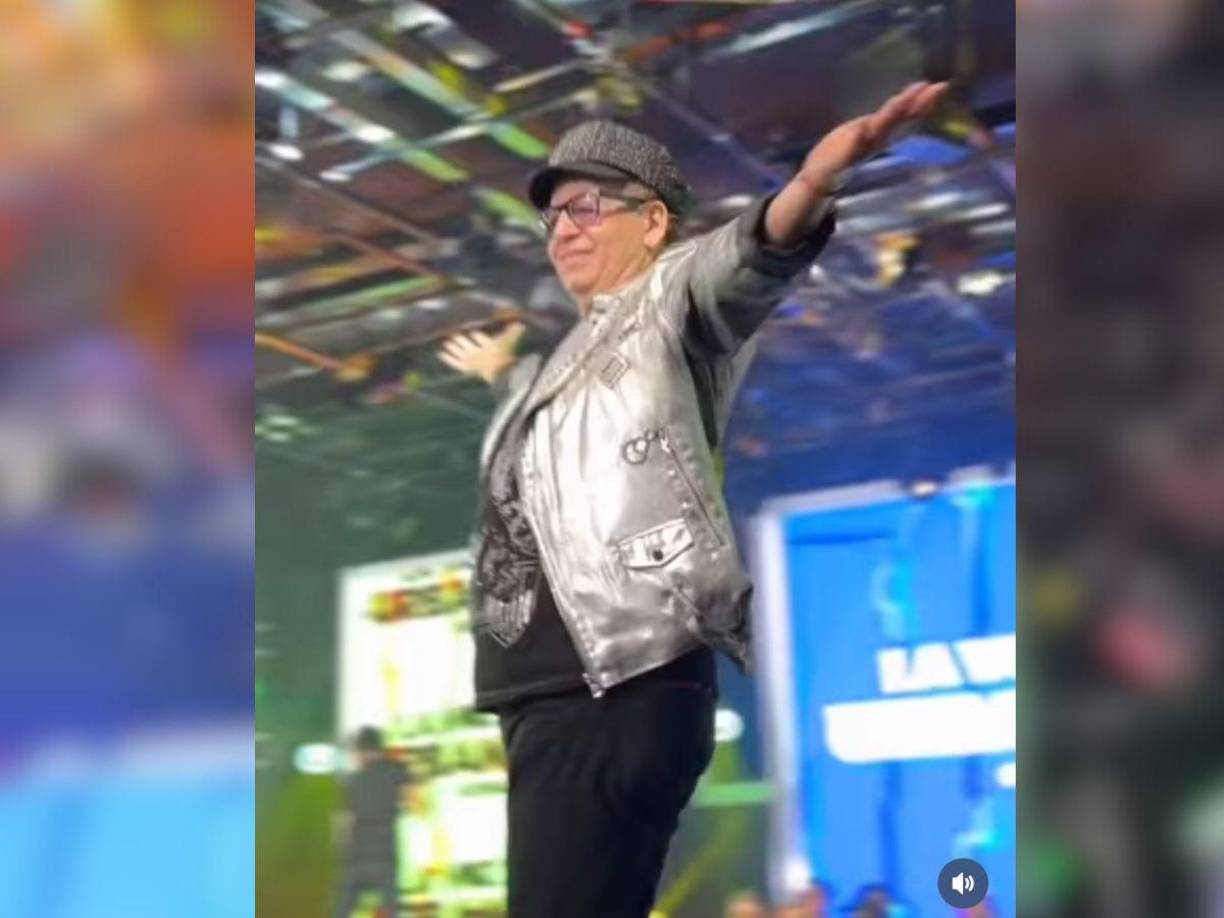 De inmediato comienza a saludar al público mientras camina hacia el frente. 