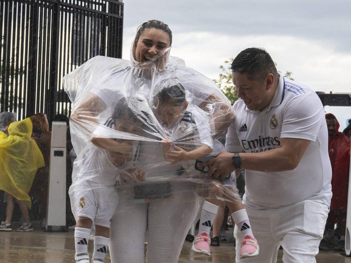 Padres de familia resguardan a sus hijos en plena tormenta. Todos ellos con la camiseta del Real Madrid.