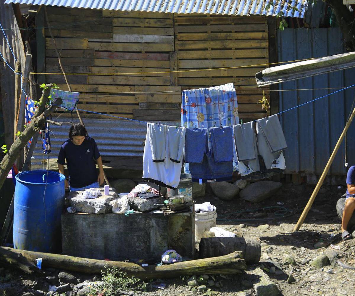 En la foto, una familia realiza labores domésticas frente a una vivienda improvisada construida con láminas y madera, en un asentamiento precario donde las condiciones de vida reflejan las carencias habitacionales que enfrentan miles de hogares en el país.