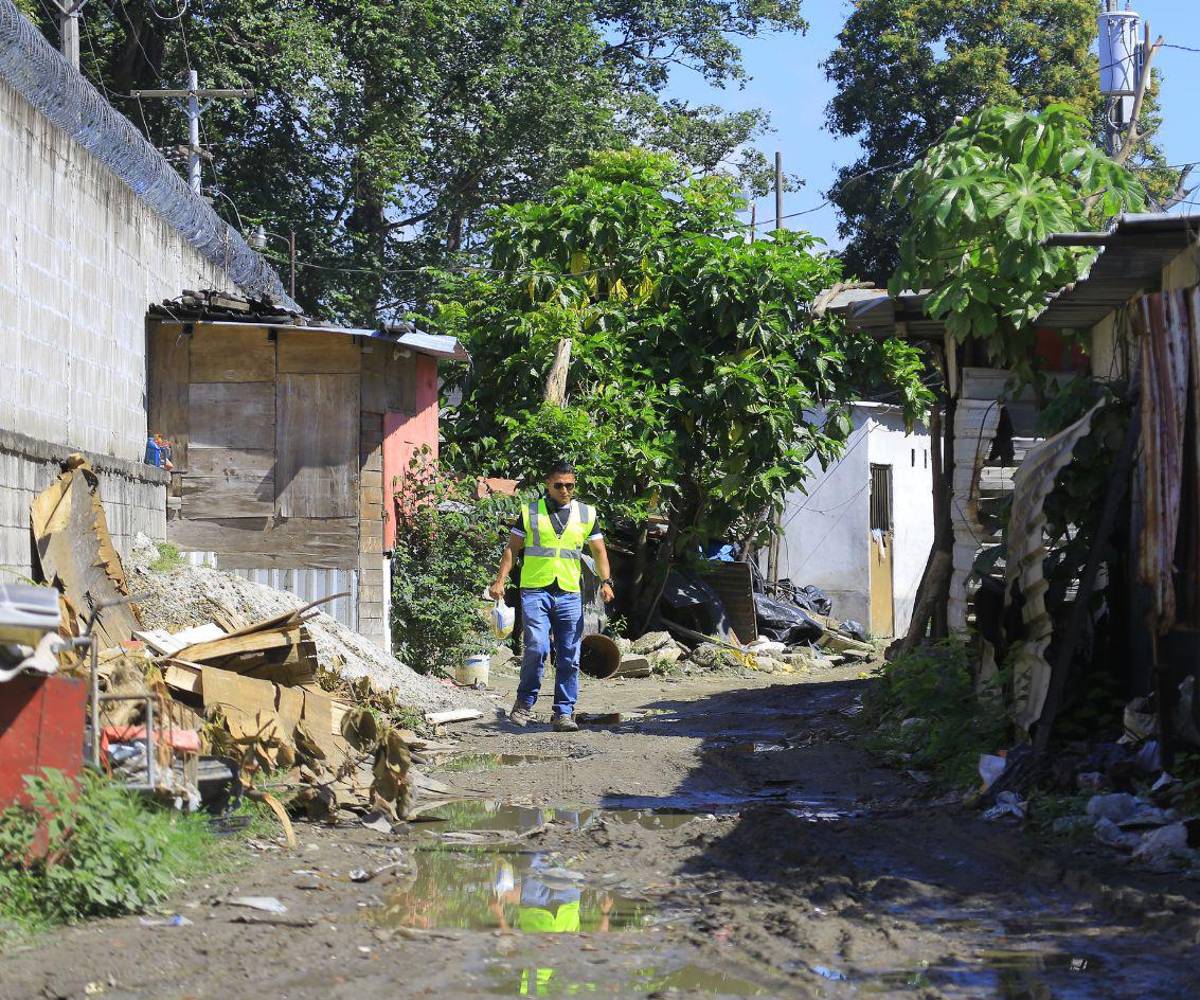 Habitante camina por un callejón de tierra entre viviendas precarias construidas con materiales improvisados, en un sector con calles deterioradas y deficiencias visibles en servicios básicos.