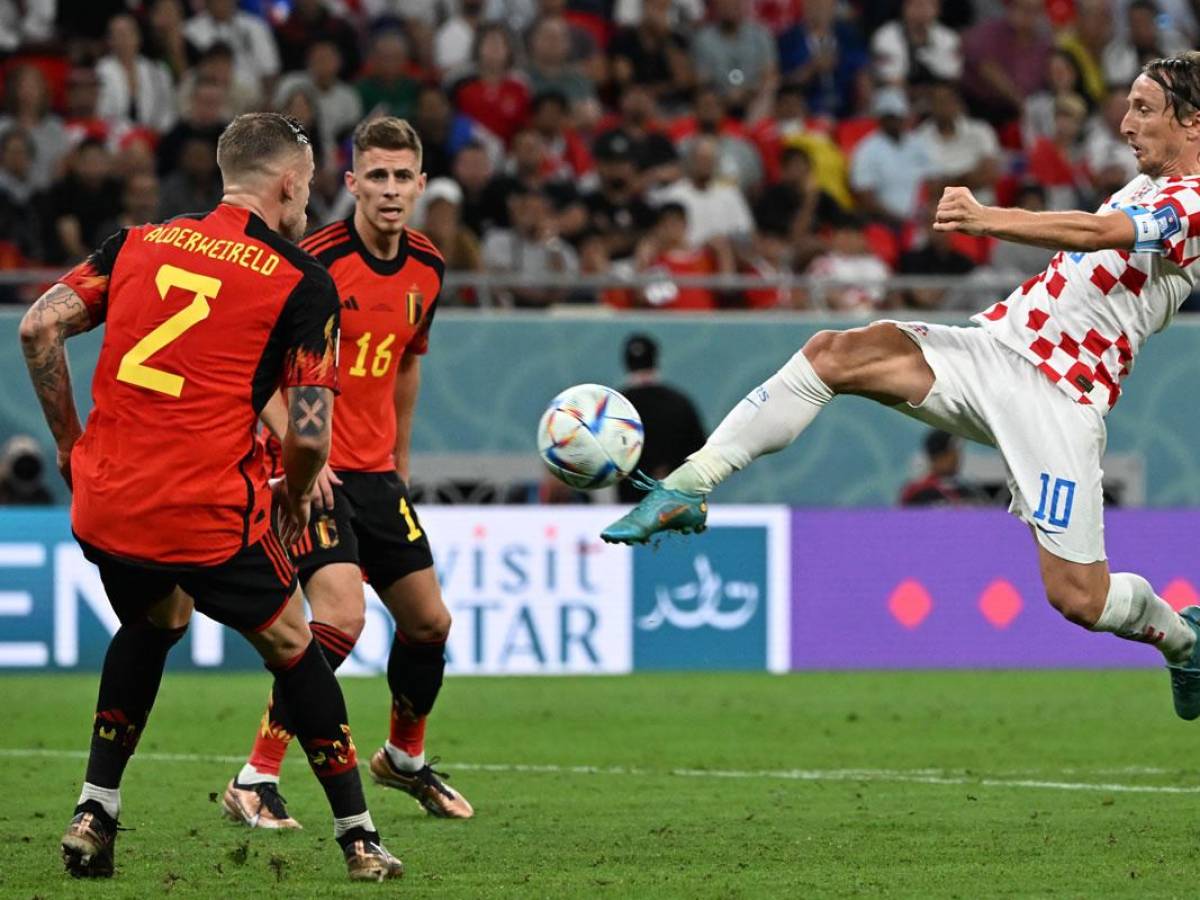 Luka Modric conecta el balón ante la mirada de dos jugadores de Bélgica.