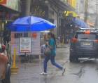 Una mujer intenta protegerse de la lluvia mientras cruza la calle en el centro de San Pedro Sula.