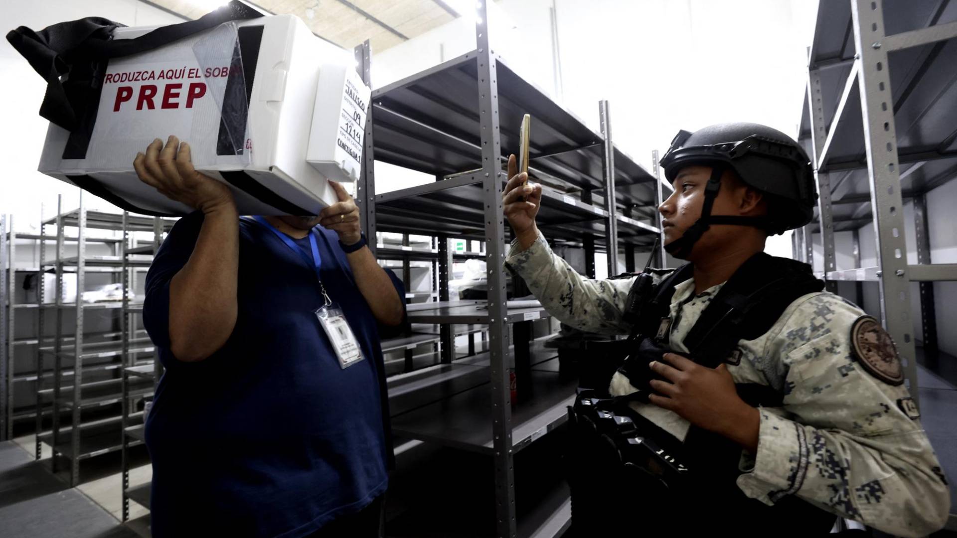 $!<b>Un miembro de la Guardia Nacional filma a un funcionario del Instituto Nacional Electoral (INE) cargando un paquete con material electoral que será utilizado en las próximas elecciones presidenciales en un distrito electoral en Guadalajara, estado de Jalisco, México, el 31 de mayo de 2024.</b>