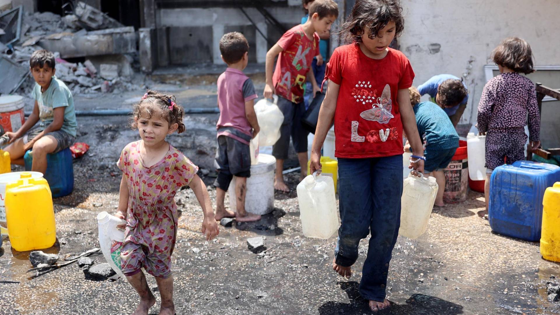 $!Niños de Gaza cargan contenedores de agua en junio cerca de una escuela usada como refugio en Jabaliya.