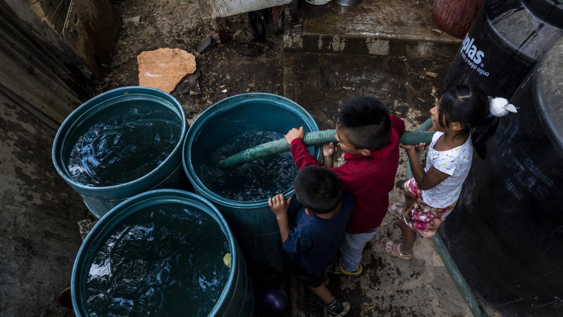 $!Niños ayudan a llenar barriles de agua del reparto semanal de agua en su barrio de la Ciudad de México.