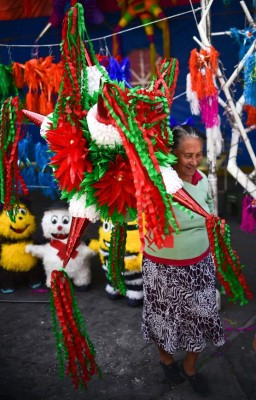 A woman carries a traditional Mexican pinata at a market in Acolman, Mexico state, on December 18, 2017. The pinata -a papier mache party decoration filled with candy that is hung up at parties and struck with a stick until it breaks open- is a central element of the Mexican Christmas holidays, forming part of a deep-rooted tradition that mixes indigenous customs and the evangelising zeal of the Augustinians in the sixteenth century. / AFP PHOTO / RONALDO SCHEMIDT / TO GO WITH AFP STORY by YEMELI ORTEGA