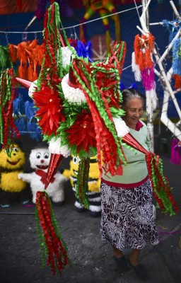 A woman carries a traditional Mexican pinata at a market in Acolman, Mexico state, on December 18, 2017. The pinata -a papier mache party decoration filled with candy that is hung up at parties and struck with a stick until it breaks open- is a central element of the Mexican Christmas holidays, forming part of a deep-rooted tradition that mixes indigenous customs and the evangelising zeal of the Augustinians in the sixteenth century. / AFP PHOTO / RONALDO SCHEMIDT / TO GO WITH AFP STORY by YEMELI ORTEGA
