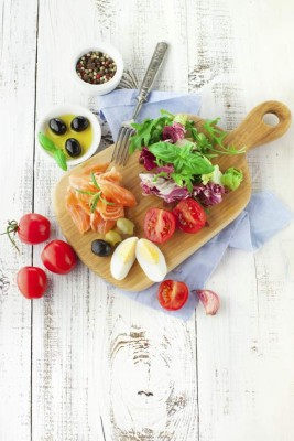 Ingredients for salad with salmon, cherry tomatoes and lettuce on a wooden chopping board on rustic white background, top view