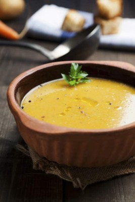 rustic soup of pumpkin and potatoes in earthenware bowl with toasted bread in the background ready on the wooden table view on the top